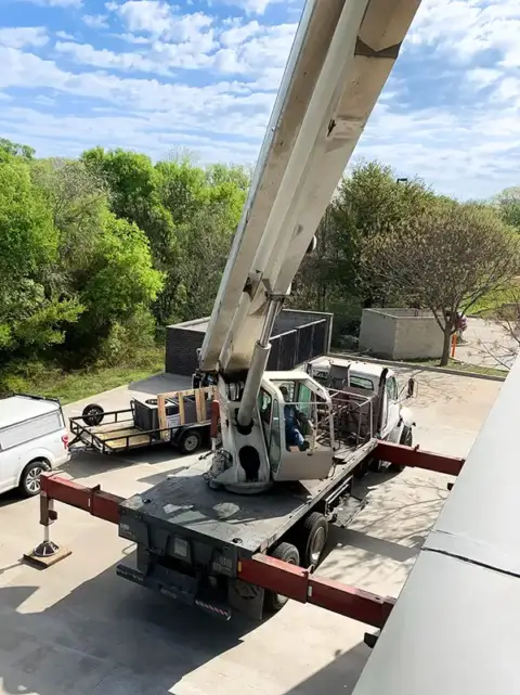 A crane lifting a commercial HVAC unit high into the air.
